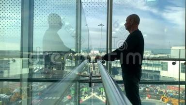 一位游客背着背包站在机场候机室明亮的大楼里，站在窗口看着街道，看着他的街道